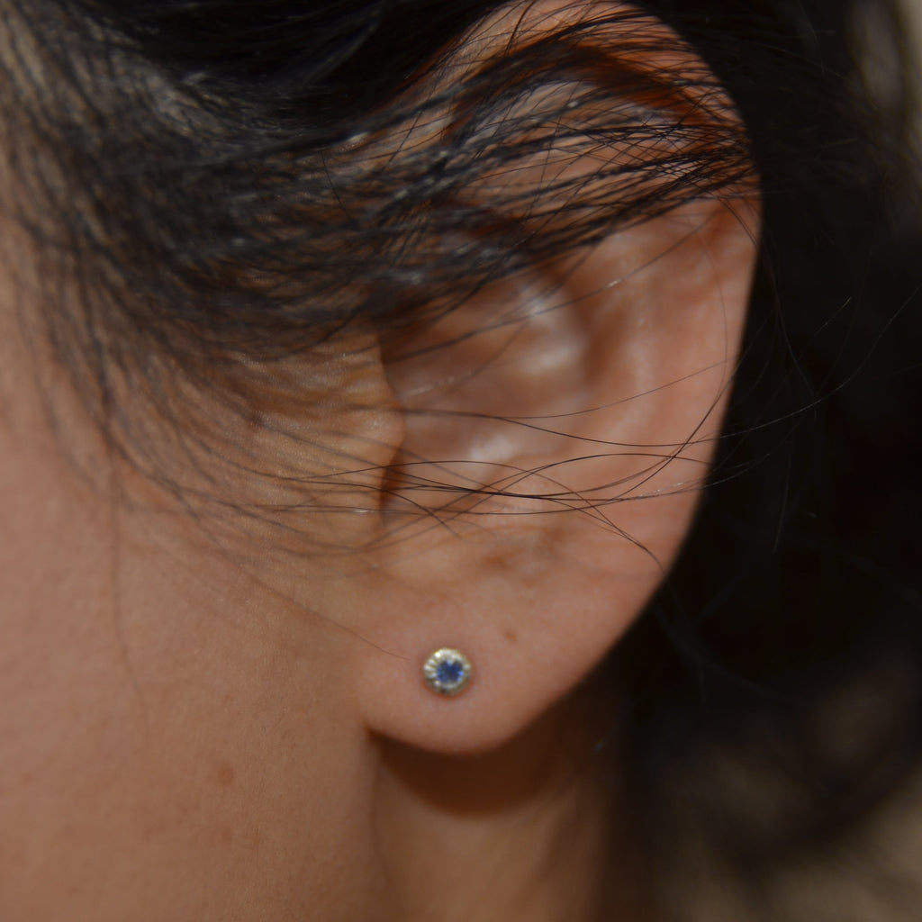 Close-up of an ear with a sapphire earring against a blurred background
