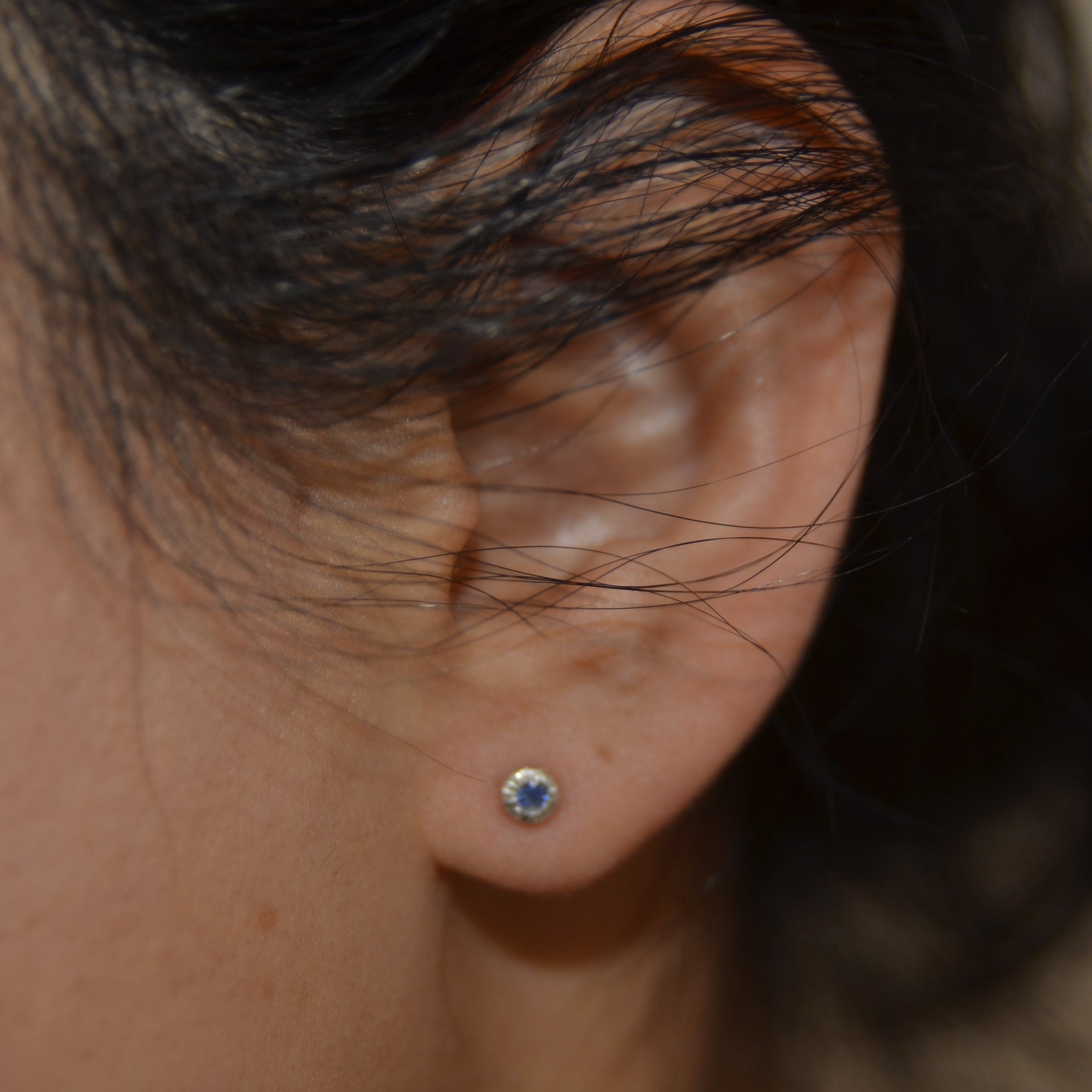Close-up of an ear with a sapphire earring against a blurred background