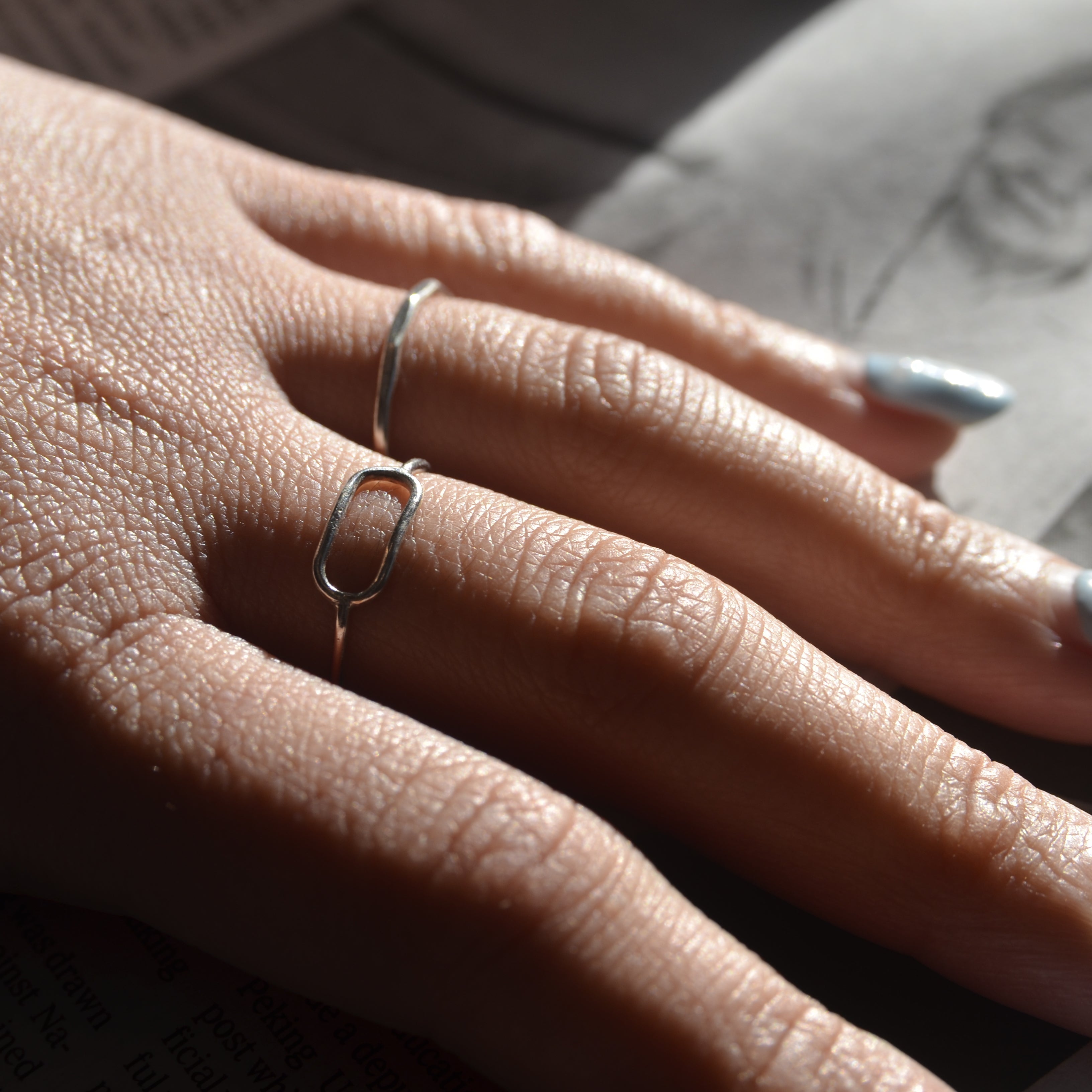 Close-up of a hand with two silver rings on a blurred background