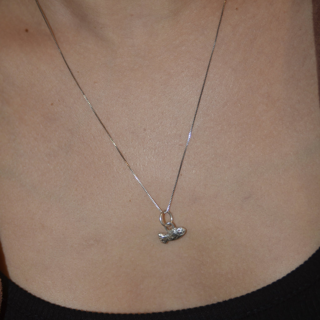 Silver fish charm being worn on a small chain