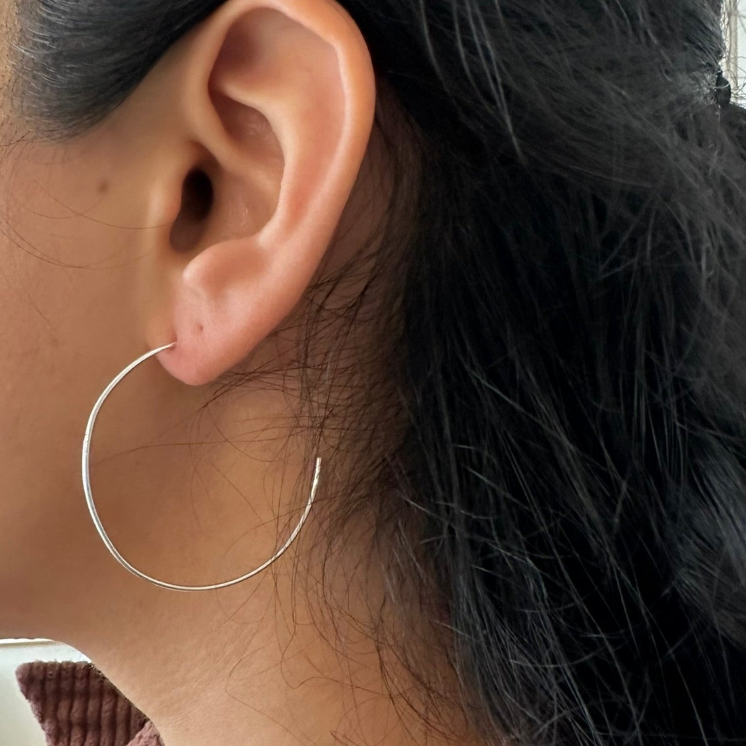 Close-up of a person wearing a silver hoop earring with a blurred background