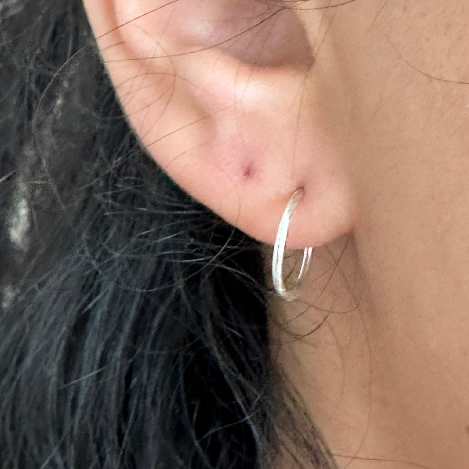 Close-up of an ear wearing a silver hoop earring with dark hair partially visible.