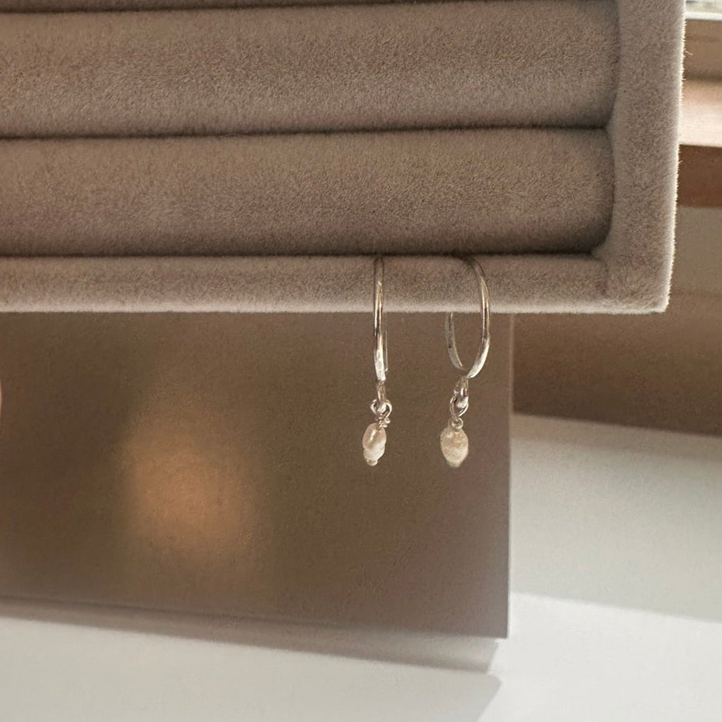Silver earrings hanging from a gray jewelry box.