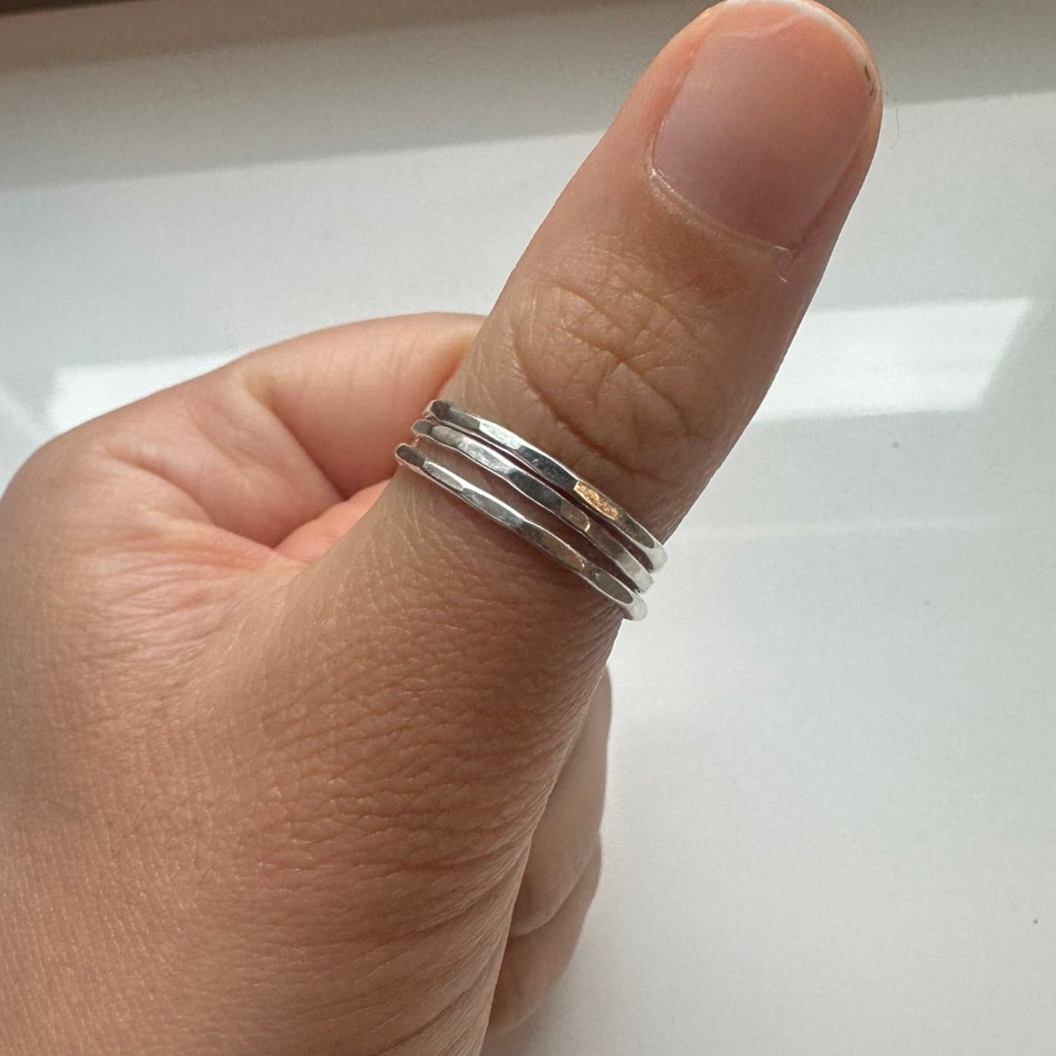 Hand wearing two silver rings on a plain background