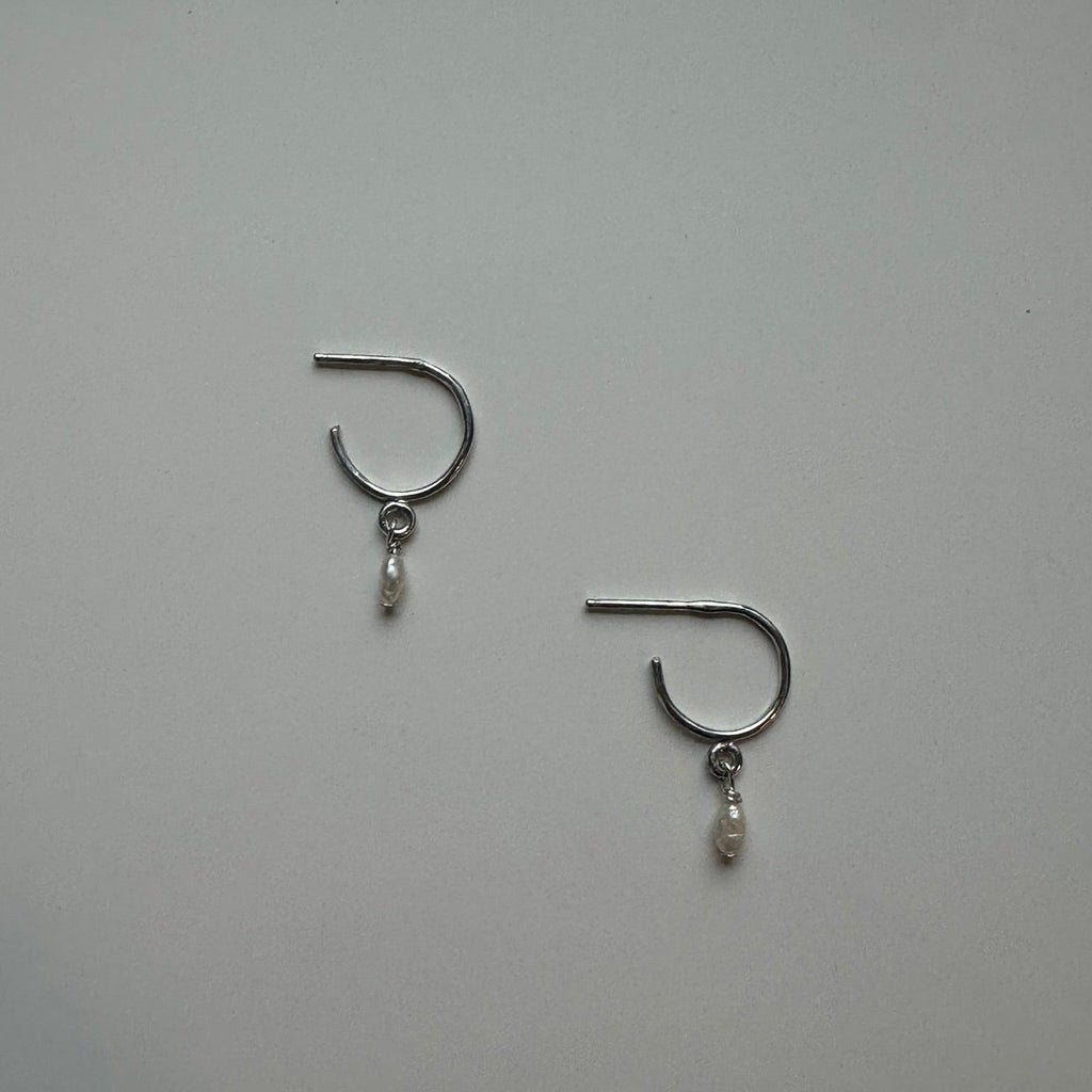 Pair of silver earrings with small dangling pearls on a light gray background