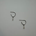 Pair of silver earrings with small dangling pearls on a light gray background